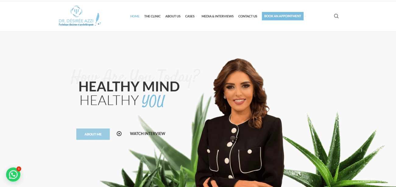 Dr. Désirée Azzi, clinical and psychoanalytic psychologist, smiling in professional attire, with green plants in the background, promoting mental health and well-being.