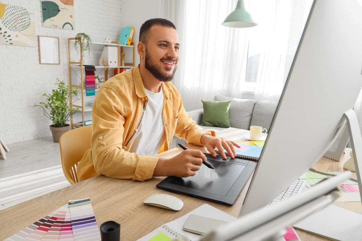 Graphic designer working at a desk with a digital tablet, creating designs in a bright workspace, showcasing elements of branding and graphic design services.